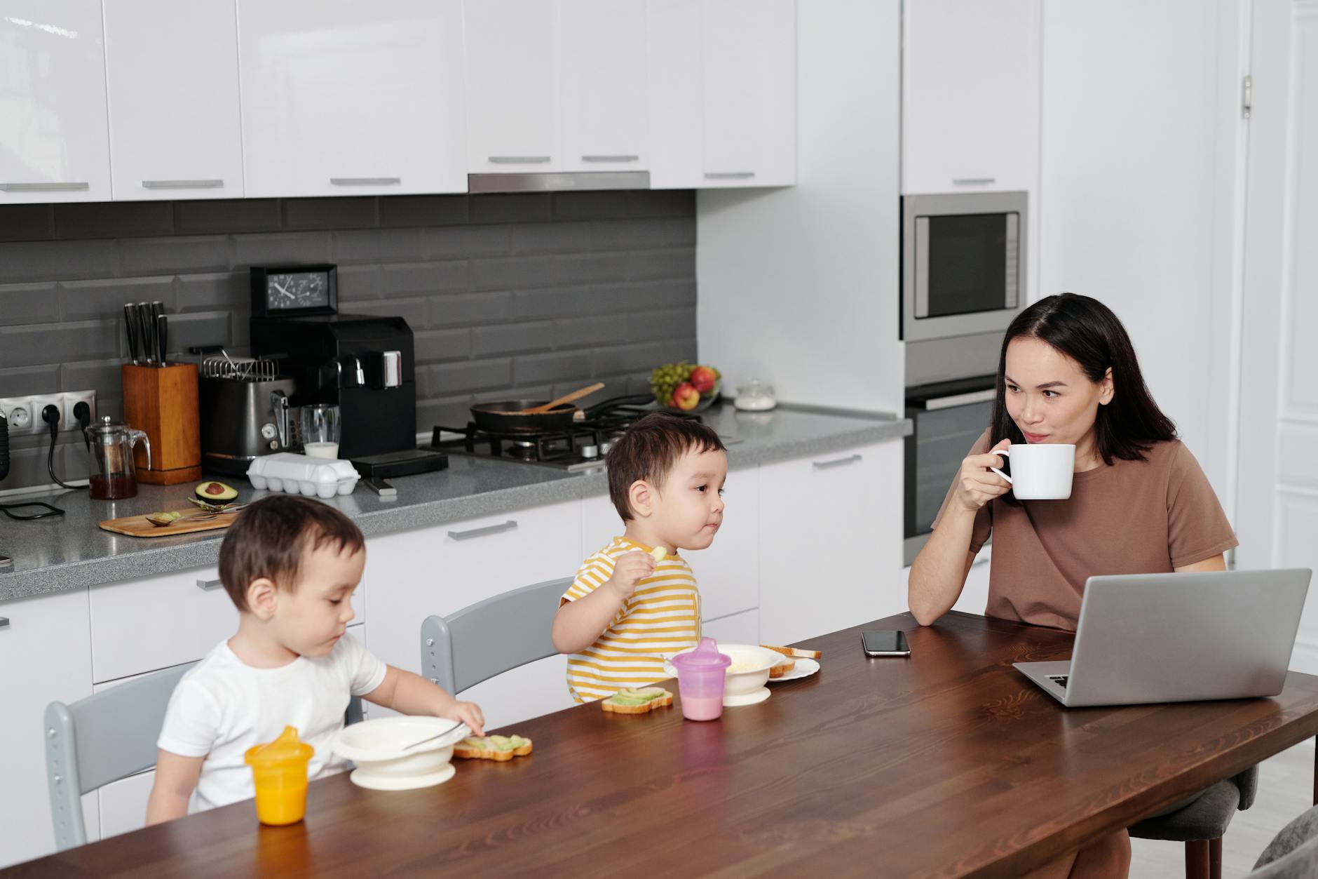 mother using laptop while sons eating meal in a kitchen